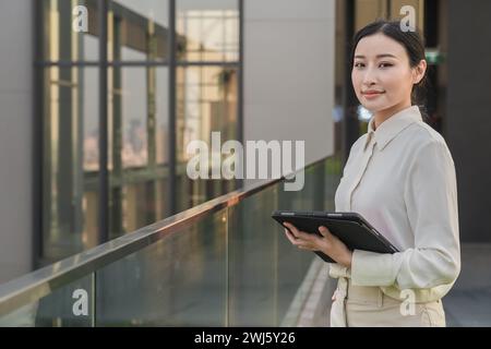 Eine junge asiatische Frau auf einem Balkon mit einer Tablette, KI-generiert. Stockfoto