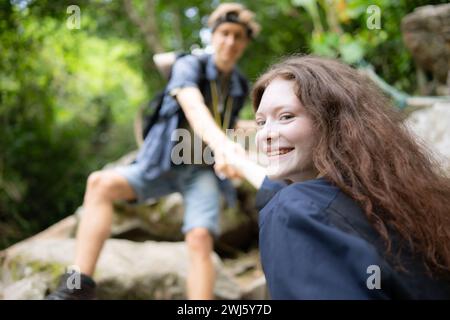 Junge Paare beim Wandern im Wald helfen einander beim Klettern, Mann und Frau beim Trekking in der Natur. Stockfoto