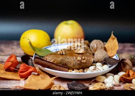 Türkischer Kuchen aus Baklava auf dem Teller, dekoriert mit frischen Pistazien, Nüssen, Zitrone, Apfel, Vanille und trockenen Herbstblättern, auf massivem Holztisch Stockfoto