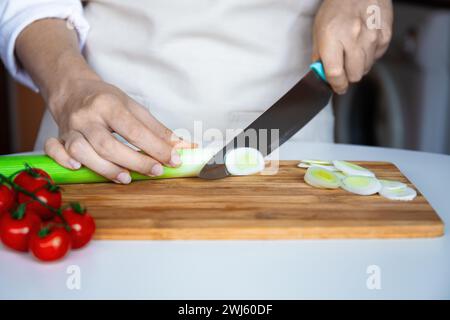 Ein Koch schneidet fachmännisch mit Messerlauch auf hölzernem Schneidebrett, mit Tomaten zur Seite. Zubereitung von Mahlzeiten, Kochen von Speisen in der Küche Stockfoto