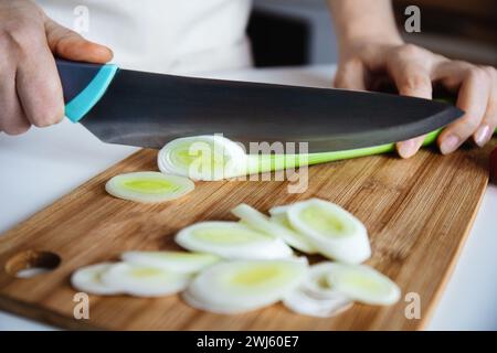 Hände eines Küchenchefs, der frischen grünen Lauch mit einem großen Küchenmesser auf einem Bambus-Schneidebrett schneidet. Stockfoto