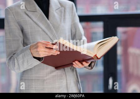 Eine unerkennbare Frau hält ein großes braunes Buch in den Händen. Geschäftsstil, Universitätslehrer Stockfoto