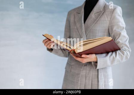 Eine unerkennbare Frau hält ein großes braunes Buch in den Händen. Geschäftsstil, Universitätslehrer Stockfoto