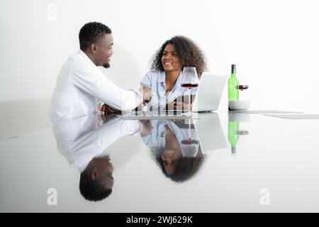 Beide jungen Unternehmen trinken Wein und nutzen ihre Laptops, um Informationen in ihrem Wohnzimmer miteinander zu teilen. Stockfoto