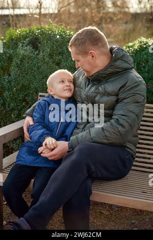 Herbstliche Familienzusammenhänge: Vater, 40 Jahre alt, und Sohn - wunderschöner 8-jähriger Junge, im Park sitzend. Stockfoto