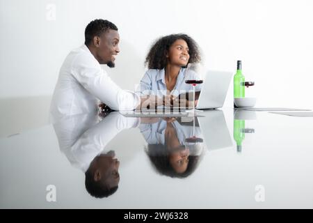 Beide jungen Unternehmen trinken Wein und nutzen ihre Laptops, um Informationen in ihrem Wohnzimmer miteinander zu teilen. Stockfoto