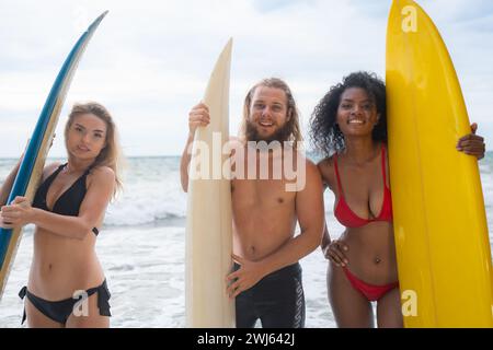 Zwei Frauen und ein junger Mann mit Surfbrettern, die bereit sind, ins Meer zu gehen, um zu surfen. Stockfoto