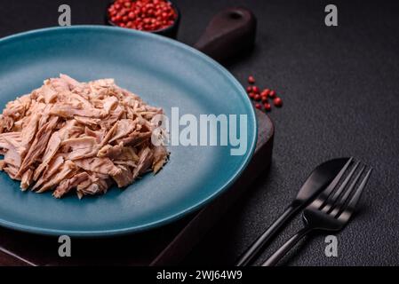 Köstliches Thunfischfleisch in Dosen mit Salz, Gewürzen und Öl auf dunklem Betonhintergrund Stockfoto