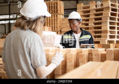 Junge weibliche und männliche Lagerarbeiter, die ein digitales Tablet für die Arbeit in einer Holzfabrik verwenden, um die Ordnung der Dielen zu überprüfen Stockfoto