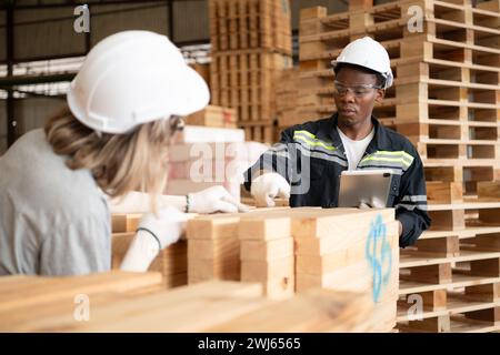 Junge weibliche und männliche Lagerarbeiter, die ein digitales Tablet für die Arbeit in einer Holzfabrik verwenden, um die Ordnung der Dielen zu überprüfen Stockfoto