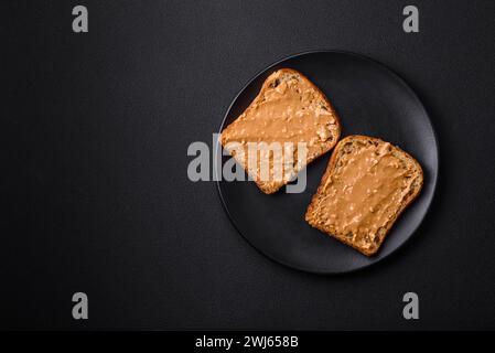 Nahrhaftes Sandwich aus Brot und Erdnussbutter auf einer schwarzen Keramikplatte Stockfoto