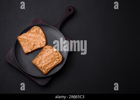 Nahrhaftes Sandwich aus Brot und Erdnussbutter auf einer schwarzen Keramikplatte Stockfoto