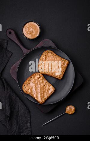 Nahrhaftes Sandwich aus Brot und Erdnussbutter auf einer schwarzen Keramikplatte Stockfoto