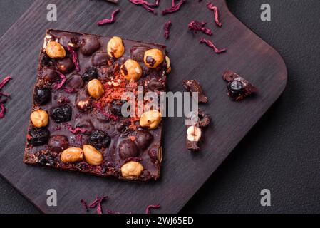 Handgemachte Schokolade mit Beeren, Nüssen und Gewürzen auf dunklem Hintergrund Stockfoto