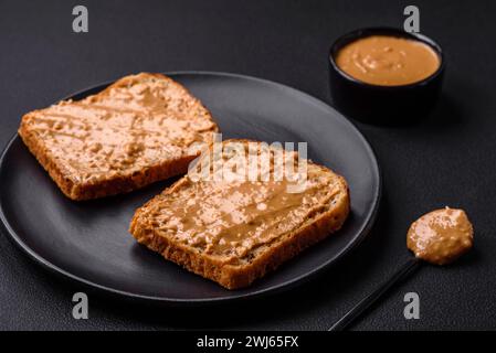 Nahrhaftes Sandwich aus Brot und Erdnussbutter auf einer schwarzen Keramikplatte Stockfoto