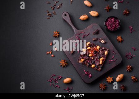 Handgemachte Schokolade mit Beeren, Nüssen und Gewürzen auf dunklem Hintergrund Stockfoto