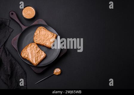 Nahrhaftes Sandwich aus Brot und Erdnussbutter auf einer schwarzen Keramikplatte Stockfoto