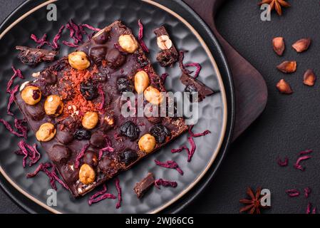 Handgemachte Schokolade mit Beeren, Nüssen und Gewürzen auf dunklem Hintergrund Stockfoto