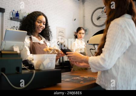 Der Barista für junge Frauen serviert Gäste, die ihre eigenen Tassen in einem Café mitbringen. Stockfoto