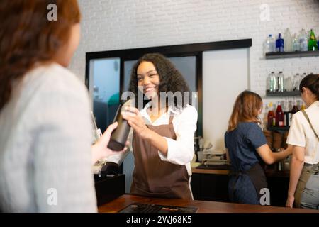 Der Barista für junge Frauen serviert Gäste, die ihre eigenen Tassen in einem Café mitbringen. Stockfoto