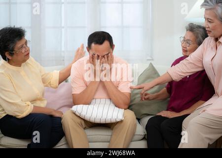 Senior asiatischer Mann, der an einer schweren Krankheit leidet, sitzt auf dem Sofa mit Freunden, die zu Besuch kommen, und ermutigt die Stockfoto