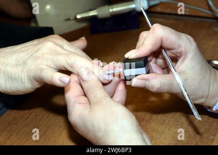 Auf dem Foto wird der Moment festgehalten, in dem ein Manikürer mit einem Pinsel Lack auf die Fingernägel des Kunden aufträgt. Stockfoto