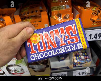 Dortmund, Deutschland - 19. Februar 2022: POV männliche Hand-Halten-Packung mit Tony's Chocolonely Toffee Schokolade mit Regalen im Supermarkt im Hintergrund Stockfoto