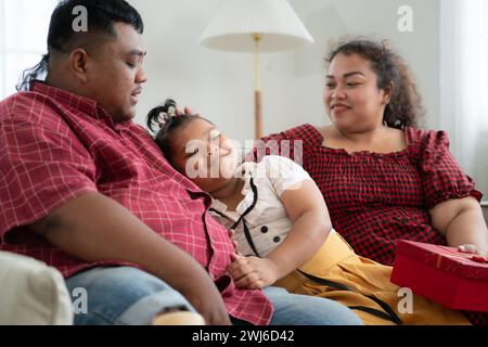 Eine große Familie mit einem Vater, der eine Beinprothese trägt, schenkt einer Tochter, die in der Schule gut geht und Anerkennung erhält Stockfoto