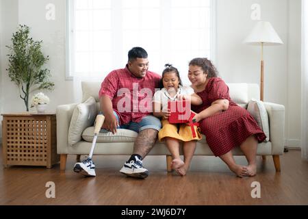 Eine große Familie mit einem Vater, der eine Beinprothese trägt, schenkt einer Tochter, die in der Schule gut geht und Anerkennung erhält Stockfoto