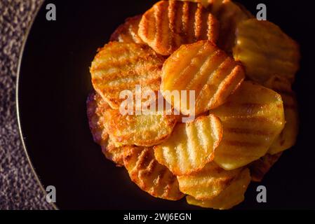 Köstliche knusprige Bratkartoffeln in Scheiben auf einer schwarzen Keramikplatte Stockfoto