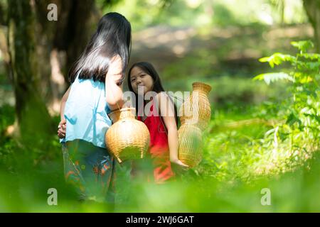 Zwei asiatische Mädchen mit traditioneller Kleidung stehen im Regenwald. Sie hatten Spaß miteinander zu spielen, bevor sie Opa halfen Stockfoto
