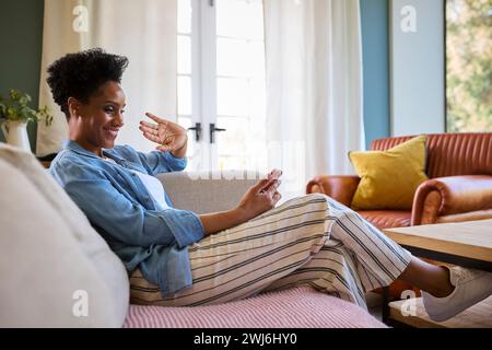 Reife Frau, Die Sich Zu Hause Auf Dem Sofa Entspannt Und Videoanrufe Auf Dem Mobiltelefon Macht Stockfoto