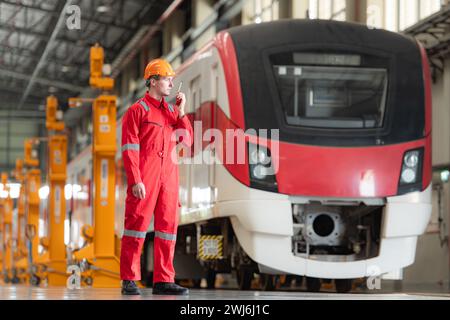 Porträt eines Technikers, der ein Walkie-Talkie vor einem Zug verwendet, um nach der Inspektion des Elektrofahrzeugs mit seinen Kollegen zu kommunizieren Stockfoto