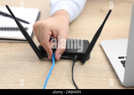 Mann, der Kabel in den WLAN-Router an einem Holztisch drinnen steckt, Nahaufnahme Stockfoto