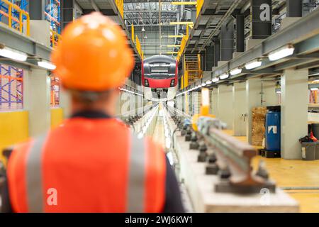 Rückansicht eines Ingenieurs der Elektrobahn mit Schutzhelm und reflektierender Weste. Es gibt ein Elektroauto im Auto R Stockfoto