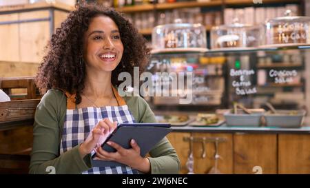 Lächelnde Junge Frau Mit Schürze, Die Im Lebensmittelgeschäft Mit Einem Digitalen Tablet Arbeitet Stockfoto