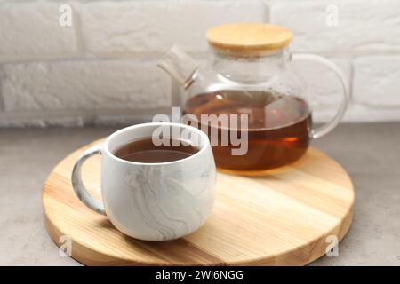 Aromatischer Tee in Glas-Teekanne und -Tasse auf grauem Tisch vor weißer Ziegelwand Stockfoto