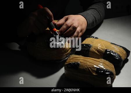 Schmuggel und Drogenhandel. Mann, der ein Paket mit Betäubungsmitteln öffnet, mit einem Koffer in der Dunkelheit, Nahaufnahme Stockfoto