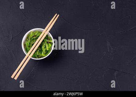 Chuka Salat auf einem weißen Teller mit chinesischen Stäbchen auf dunklem Hintergrund. Kopierbereich, Draufsicht Stockfoto