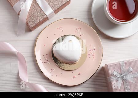 St. Valentinstag. Köstlicher herzförmiger Kuchen, Tee und Geschenk auf weißem Holztisch, flach gelegen Stockfoto