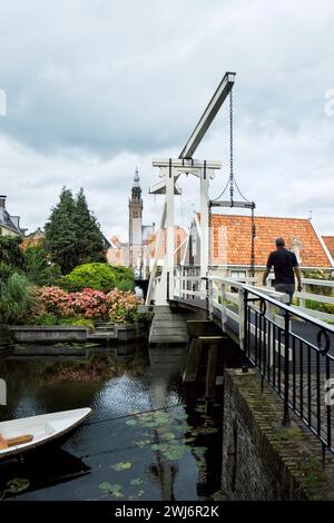Ein Mann geht über die Kwakelsteeg Brücke in alte Stadt Edam, Nord-Holland, der Kirchturm der Kleine Kerk in Ferne zu sehen. Stockfoto
