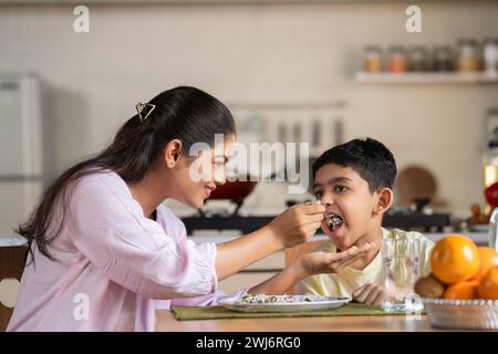 Glückliche indische Mutter, die ihr Kind zu Hause auf dem Esstisch ernährt - Konzept der elterlichen Betreuung, Familienbindung und Mutterschaft. Stockfoto