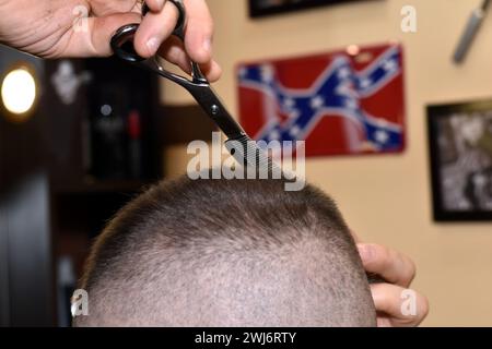 Das Bild zeigt einen Mann, der sich in einem Salon die Haare schneiden lässt. Ein Friseur verwendet eine Schere, um Haare vom Kopf eines Kunden zu entfernen. Stockfoto