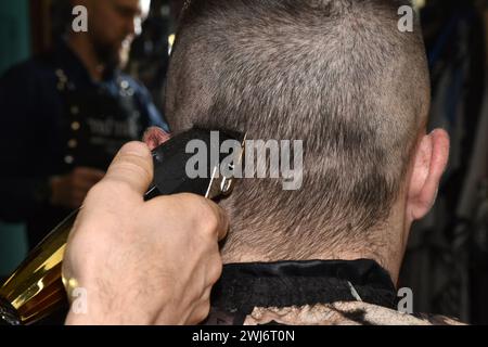 Haare schneiden in einem Salon am Kopf eines Mannes. Ein Friseur verwendet eine elektrische Maschine, um Haare vom Hinterkopf eines Kunden zu entfernen. Stockfoto