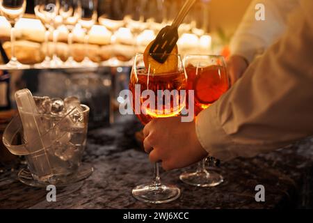 Der Barkeeper macht zwei Gläser Cocktail Aperol Spritz an der Bar und fügt frische Orangenscheiben hinzu. Typisch italienisches alkoholisches Getränk, Aperitif mit Stockfoto