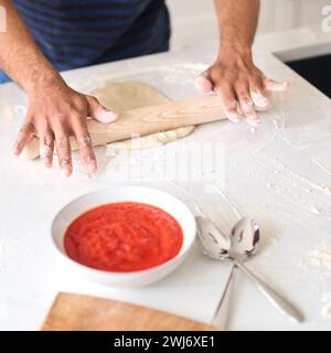 Nahaufnahme Von Mann Zu Hause, Der Teig Für Hausgemachte Pizza In Der Küche Ausrollen Lässt Stockfoto