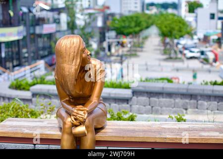 Gangneung City, Südkorea - 29. Juli 2019: Eine goldene Statue einer jungen Frau sitzt auf einer Parkbank mit Blick auf die Wolhwa Street im Zentrum von Gangneung. Stockfoto