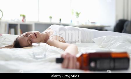 Betrunkene Frau schläft allein auf einem Bett mit einer Flasche Stockfoto