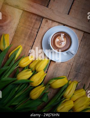 Kaffeetasse mit gelben Tulpenblüten und Noten von Guten Morgen auf blauem rustikalem Tisch von oben, Frühstück am Mütter- oder Frauentag Stockfoto