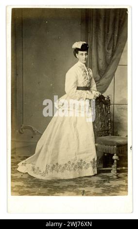 Originale viktorianische Carte de Visite (Visitenkarte oder CDV) einer feinen eleganten, wunderschönen Dame in wunderschönem Kleid mit einem Zug in zwei Teilen - einem Rock und einem Paletot (oder Jacke). Ihr Haar ist mit einem Knotenbrötchen und einem kleinen Hut mit Federn gekleidet. Aus dem Studio von William Bartholomew, Egham, Surrey, Großbritannien um 1868, 1869. Stockfoto